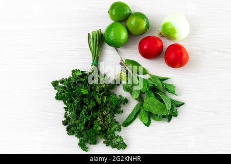 Bündeln und Minzpakete mit Zitronen, Tomaten und Zwiebeln auf weißem, strukturiertem Holzhintergrund Stockfoto