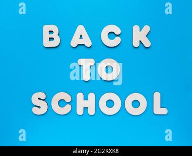 Inschrift ZURÜCK ZUR SCHULE aus Holzbuchstaben auf blauem Hintergrund. Das Konzept der Bedeutung von Bildung. Stockfoto