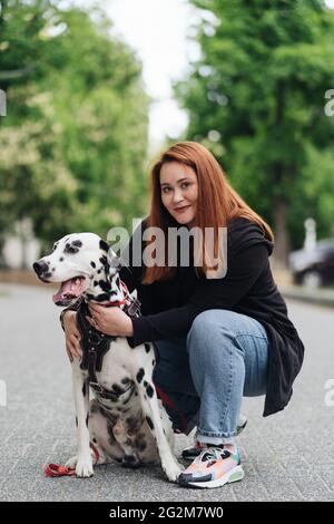 Glückliche Frau posiert und spielt mit ihrem dalmatinischen Hund während eines Stadtspaziergangs. Freundschaft, Liebe und Fürsorge Konzept Stockfoto