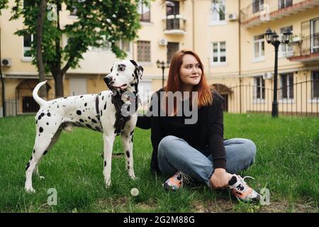 Glückliche Frau posiert und spielt mit ihrem dalmatinischen Hund während eines Stadtspaziergangs. Freundschaft, Liebe und Fürsorge Konzept Stockfoto