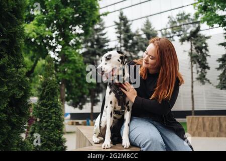 Glückliche Frau posiert und spielt mit ihrem dalmatinischen Hund während eines Stadtspaziergangs. Freundschaft, Liebe und Fürsorge Konzept Stockfoto