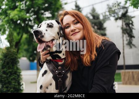 Glückliche Frau posiert und spielt mit ihrem dalmatinischen Hund während eines Stadtspaziergangs. Freundschaft, Liebe und Fürsorge Konzept Stockfoto