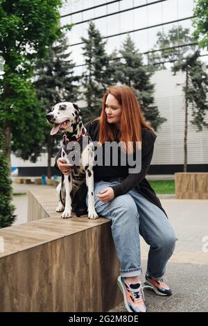 Glückliche Frau posiert und spielt mit ihrem dalmatinischen Hund während eines Stadtspaziergangs. Freundschaft, Liebe und Fürsorge Konzept Stockfoto