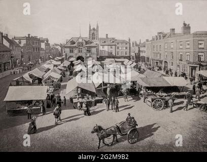 Ein Blick aus dem späten 19. Jahrhundert auf den Markt am Marktplatz, Peterborough, einer Domstadt in Cambridgeshire, England. Es war die Eröffnung der Linie der Great Northern Railway von London nach York im Jahr 1850, die Peterborough von einer Marktstadt in ein Industriezentrum verwandelte und den Großteil des 20. Jahrhunderts zum führenden britischen Ziegelhersteller wurde. Die Ziegelherstellung war seit dem frühen 19. Jahrhundert ein kleines saisonales Handwerk, aber während der 1890er Jahre hatten erfolgreiche Experimente in Fletton mit den härteren Tonen aus einer niedrigeren Ebene zu einem viel effizienteren Prozess geführt. Stockfoto