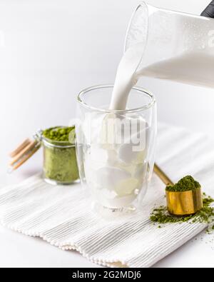 Milch in Glas gießen, um Matcha-Latte-Tee zuzubereiten Stockfoto