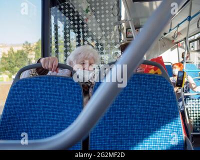 Moskau. Russland. 4. Juni 2021. Eine alte grauhaarige Frau in einer Schutzmaske sitzt am Fenster in einem Stadtbus. Schutz der Passagiere vor Viren Stockfoto