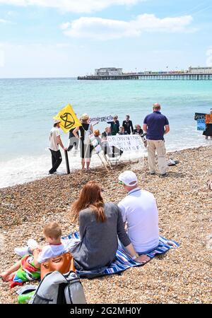 Worthing Sussex UK 12. Juni 2021 - Besucher beobachten, wie Aktivisten des Extinction Rebellion heute an einem Protest am Worthing Beach teilnehmen, der im Rahmen eines Aktionswochenendes anlässlich des G7-Gipfels die Auswirkungen des Klimawandels und des steigenden Meeresspiegels beleuchtet: Credit Simon Dack / Alamy Live News Stockfoto