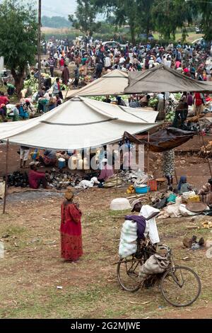 Kasese, Uganda - Juli 22 2011: Menschenmenge auf einem lokalen, ländlichen Markt in Afrika. Schwarze Frauen und Männer Einkaufen, kaufen und verkaufen Lebensmittel, mit Fahrrad als Stockfoto