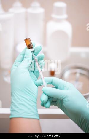 Kosmetikerin Hände mit Handschuhen Füllen einer Lipolyse in eine Spritze aus einer Flasche auf dem Hintergrund der Gläser mit kosmetischer Creme, Nahaufnahme. Stockfoto