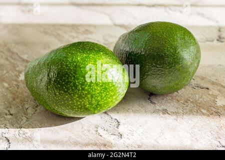 Zwei frische grüne ganze Avocados auf dem Tischhintergrund in der Küche. Stockfoto