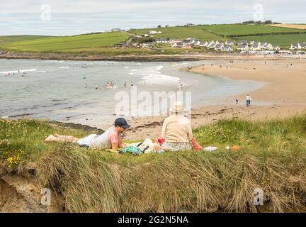 Garrettstown, Cork, Irland. Juni 2021. Ein junges Paar sitzt und liest auf den Grashängen mit Blick auf den Strand in Garrettstown, Co. Cork, Irland. - Credit; David Creedon / Alamy Live News Stockfoto