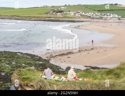 Garrettstown, Cork, Irland. Juni 2021. Ein junges Paar sitzt und liest auf den Grashängen mit Blick auf den Strand in Garrettstown, Co. Cork, Irland. - Credit; David Creedon / Alamy Live News Stockfoto
