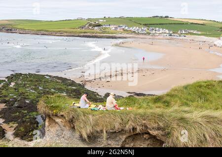 Garrettstown, Cork, Irland. Juni 2021. Ein junges Paar sitzt und liest auf den Grashängen mit Blick auf den Strand in Garrettstown, Co. Cork, Irland. - Credit; David Creedon / Alamy Live News Stockfoto