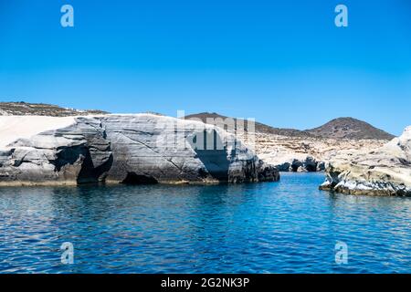 Sarakiniko auf der Insel Milos, Kykladen Griechenland. Mondlandschaft. Weiße Felsformationen, Klippen und Höhlen, blaues, gewelltes Meer und klarer Himmel im Hintergrund Stockfoto