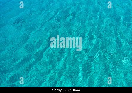 Meeresoberfläche türkisblaue Farbe Hintergrund, einige Reflexionen. Ruhiges, kristallklares Wasser mit kleinen Wellen, Sommerurlaub im tropischen Paradies. Stockfoto