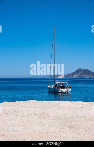 Segelboot vor Anker in Sarakiniko. Insel Milos, Griechenland. Weißer kalkhaltiger Fels, ruhiges, geriffeltes Meer und klarer blauer Himmel. Segeln in der Ägäis, Stockfoto