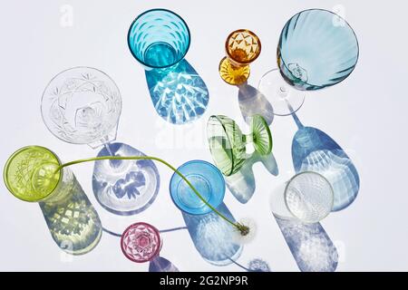 Sommerstill-Szene. Glitzernde Gläser Wasser oder Cocktails auf weißem Tischhintergrund bei Sonnenlicht. Lange harte Schatten. Urlaubskonzept Stockfoto