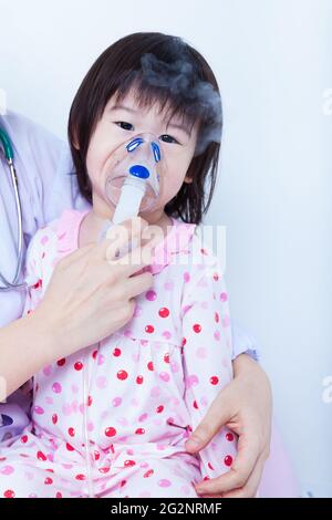 Der Arzt hilft kleinen asiatischen (thailändischen) Mädchen, die Atemwege (Kind war Bronchitis), Inhalationstherapie, Kind schaut auf die Kamera, auf weißem Hintergrund Stockfoto