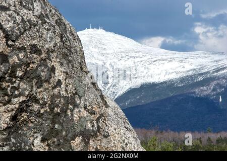 Hugh Boulder (unregelmäßig) umrahmt den schneebedeckten Gipfel des Mount Washington in New Hampshire mit Antennen des Wetterobservatoriums, die auf dem Berggipfel sichtbar sind. Stockfoto