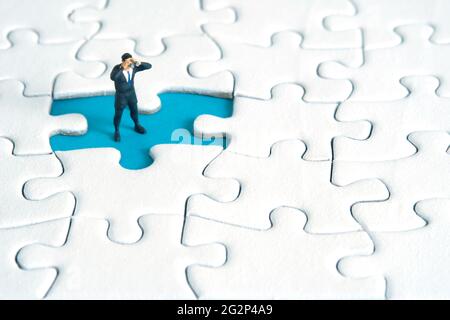 Geschäftsleute stehen über fehlende Puzzle mit Fernglas. Miniatur kleine Menschen Spielzeug Fotografie. Stockfoto