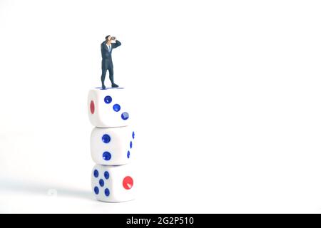 Miniatur Menschen Spielzeug Fotografie. Ein Geschäftsmann schaut, sucht, beobachtet mit einem Fernglas über den Würfeln isoliert auf weißem Hintergrund. Stockfoto