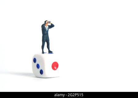 Miniatur Menschen Spielzeug Fotografie. Ein Geschäftsmann schaut, sucht, beobachtet mit einem Fernglas über den Würfeln isoliert auf weißem Hintergrund. Stockfoto
