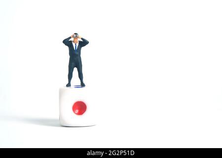 Miniatur Menschen Spielzeug Fotografie. Ein Geschäftsmann schaut, sucht, beobachtet mit einem Fernglas über den Würfeln isoliert auf weißem Hintergrund. Stockfoto