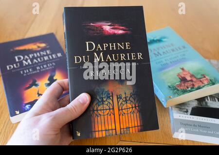 Eine Männerhand mit einem Taschenbuch von Rebecca, einem gotischen Roman der englischen Autorin Daphne du Maurier aus dem Jahr 1938 Stockfoto