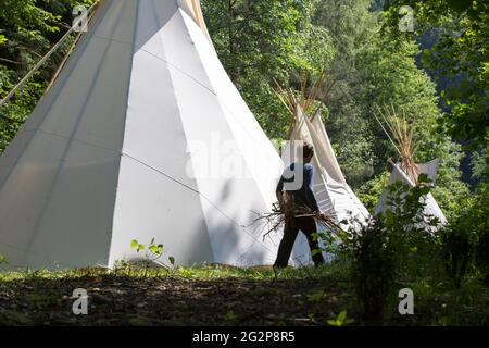 Ein Teenager mit Feuerholz in den Händen vor Tipis in einem Sommerlager in Gemany Stockfoto