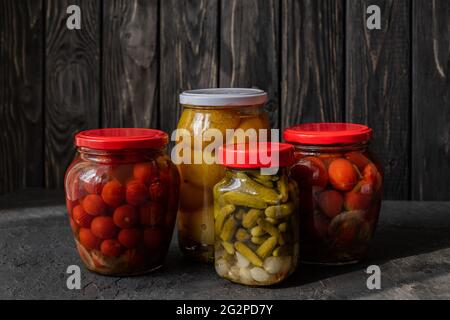Fermentierte rote und gelbe Tomaten und Gurken auf dunklem Grund. Vegetarische Gerichte. Gesalzene Tomaten und Gurken. Eingelegte Bio-Tomaten. Homema Stockfoto