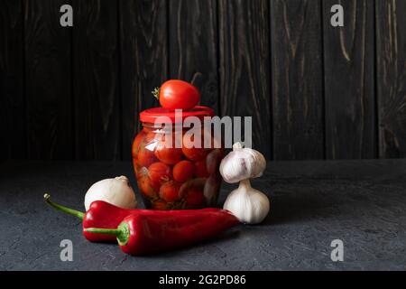 Fermentierte rote Tomaten, roter Pfeffer und Knoblauch auf dunklem Grund. Vegetarische Gerichte. Gesalzene Tomaten. Eingelegte Bio-Tomaten. Hausgemachte Gärung Stockfoto