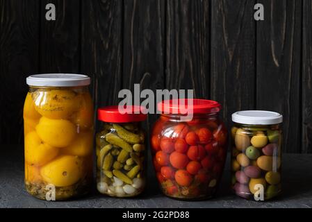 Fermentierte rote und gelbe Tomaten, Oliven und Gurken auf dunklem Grund. Vegetarische Gerichte. Gesalzene Tomaten, Oliven und Gurken. Gebeizt organisch. Stockfoto