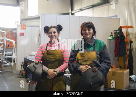 Porträt zweier Schweißer, die Schweißmasken in den Händen halten und sich auf harte Arbeit in einer Fabrik vorbereiten Stockfoto