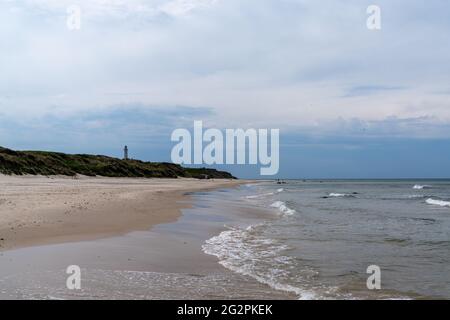 Ein wunderschöner weißer Sandstrand mit einem Leuchtturm im Hintergrund hoch oben auf grasbewachsenen Sanddünen Stockfoto