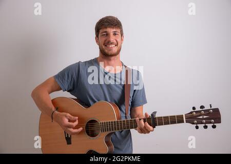 Porträt eines jungen Musikers, der Gitarre spielt und lächelt. Studiofoto eines Künstlers isoliert auf weißem Hintergrund. Junger lächelnder Mann.