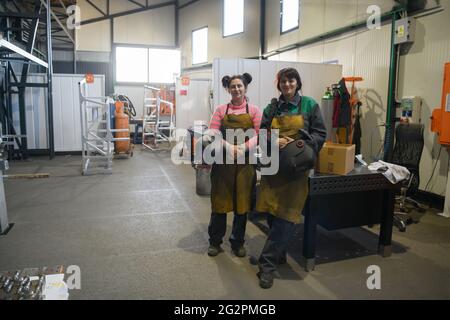 Porträt zweier Schweißer, die Schweißmasken in den Händen halten und sich auf harte Arbeit in einer Fabrik vorbereiten Stockfoto