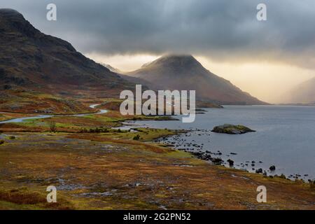 Ländliche eingleisige Straße, die durch die dramatische Landschaft des Lake District führt, mit schönem Licht, das durch Sturmwolken bricht. Stockfoto