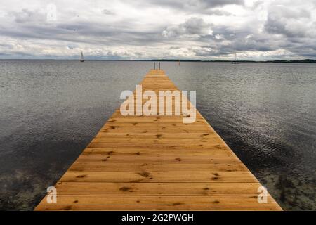 Ein Blick auf einen langen hölzernen Pier, der in das klare Meer mit Segelbooten hinter sich führt Stockfoto