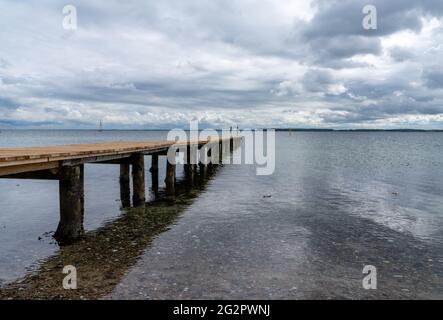 Ein Blick auf einen langen hölzernen Pier, der in das klare Meer mit Segelbooten hinter sich führt Stockfoto