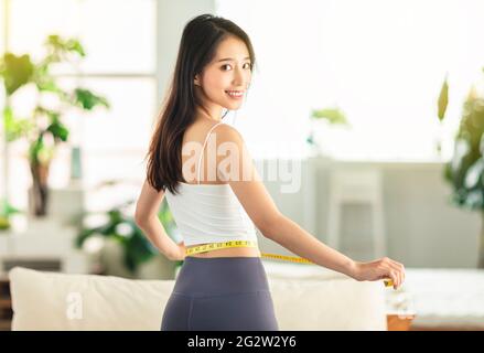 Junge Frau, die beim Tanzen einen Maßlineal hält, sich umdreht, sehr zufrieden mit ihrer Haltung, sehr glücklich, Gewicht zu verlieren Stockfoto