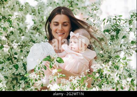 Portret niedlich schöne junge glückliche Mutter in einem weißen Hemd hält ihre sechs Monate alte Tochter in einem rosa Kleid. Glückliche Mutterschaft und glückliche Kindheit. P Stockfoto