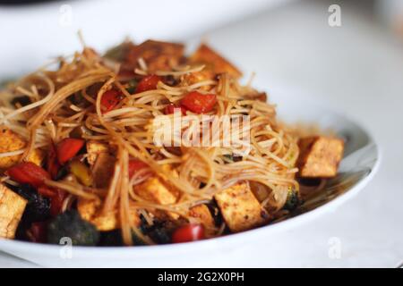 Eine große Schüssel mit asiatischer Pasta mit Paprika, Brokkoli, Tomaten, einer roten Sauce und gerösteten Tofu-Würfeln. Stockfoto