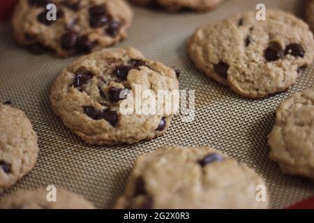 Eine Charge frischer Schokoladenkekse, die auf einer Silpat-Cookie-Matte aus Silikon kühlen, warten darauf, von der Familie verschlungen zu werden. Stockfoto