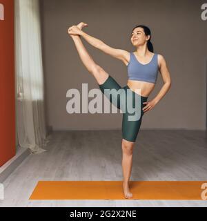 Die junge Trainerin, die Yoga praktiziert, steht im Studio auf der Matte und führt die Übung Uttita hasta padangusthasana 2 durch. Stockfoto