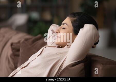 Ruhige junge indische Dame, die sich im Wohnzimmer auf dem Sofa zurücklehnen kann Stockfoto