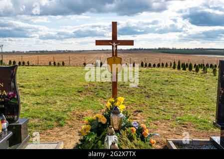 Ein hölzernes Kreuz mit einer Jesusfigur mit einem Namensschild ohne Inschriften, das auf einem frischen Erdgrab steht. Stockfoto