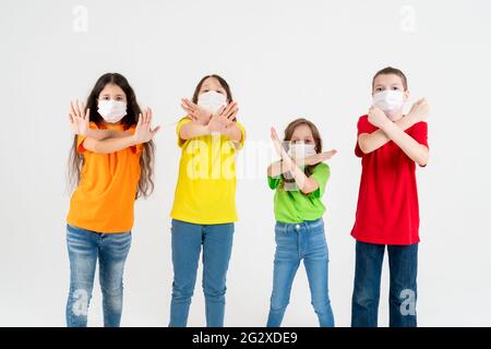 Eine Gruppe von Schulkindern in bunten T-Shirts und medizinischen Masken, die gekreuzte Hände zeigen, während sie auf die Kamera über weißem Hintergrund blicken Stockfoto