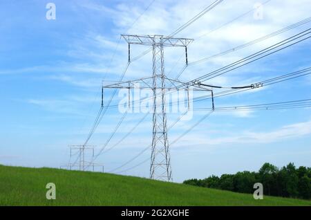 Hochspannungs-elektrische Türme und Linien mit blauem Himmel und grüner Wiese. Eleetricity Türme auf einem grünen Feld. Hochspannungsübertragungsleitungen. Stockfoto