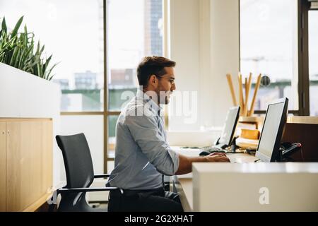 Seitenansicht eines jungen, am Computer arbeitenden Führungskräften im Büro. Geschäftsmann, der im Büro am Computer arbeitet. Stockfoto