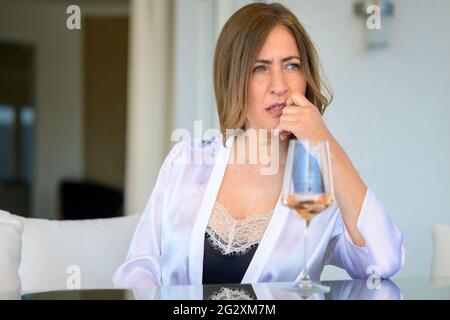 Introspective Frau sitzt tief in Gedanken an einem Patio Tisch mit einem Glas Wein ruht ihr Kinn auf der Hand starrte zur Seite mit einem Blick von konzentrat Stockfoto